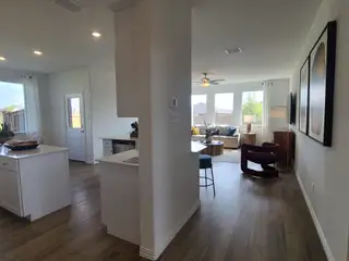 Model Home An open-concept living space with sleek wood floors, a bright kitchen island, and large windows inviting natural light.