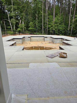 Model Home A pool construction site surrounded by lush trees, offering a glimpse of future luxury in a serene backyard setting.