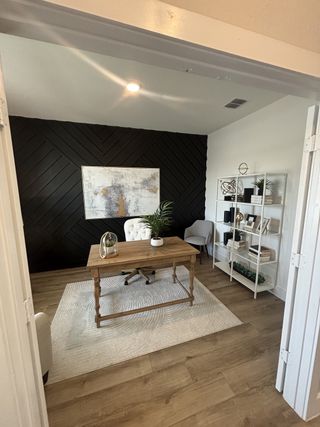 Model Home A sophisticated home office with a dark accent wall, wood flooring, and a classic desk setup for productivity.