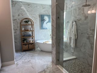 A luxurious bathroom with marble tiles, a freestanding tub, glass shower, and elegant decor.