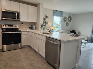Modern kitchen with sleek white cabinets, stainless steel appliances, and an open living area filled with natural light.