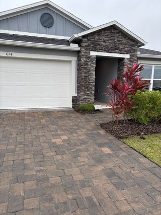 A charming home with stone accents and a paved driveway in Gardens at Waterstone I by KB Home (Palm Bay, FL).