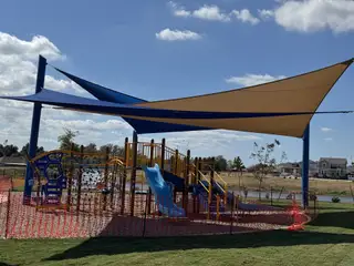 A vibrant playground with shade sails and colorful equipment in The Hills at Avery Centre by Century Communities (Round Rock, TX).