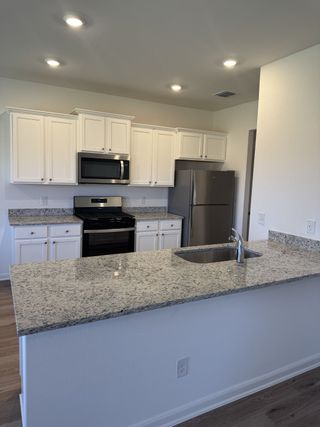 A modern kitchen with granite countertops, white cabinets, stainless steel appliances, and recessed lighting.