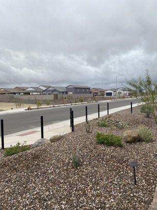 A wide street lined with modern homes featuring neutral tones and desert landscaping under a cloudy sky in Aloravita South by Taylor Morrison (Peoria, AZ).