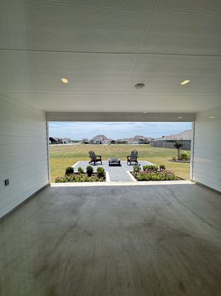 A spacious covered patio leading to a landscaped seating area with Adirondack chairs and stone path.