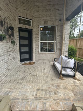 Model Home A welcoming porch with a stylish brick finish, swing bench, and wall decor adds charm and relaxation to the entrance.