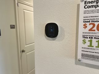 A modern thermostat on a textured wall next to an energy-saving comparison chart, showcasing home efficiency.