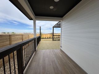 A cozy patio with wood tile flooring, black railing, and a view of a fenced yard under a spacious pergola.