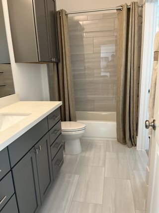 A contemporary bathroom with sleek gray cabinetry, light tile flooring, and a tub with elegant neutral curtains.