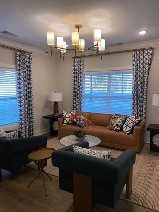 Model Home A cozy living room with a tan sofa, patterned curtains, and chic lighting, featuring a modern coffee table and decorative pillows.