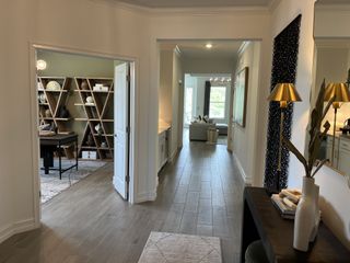 Model Home A modern hallway with sleek wood floors, a chic office, and stylish decor accents leading to a bright living area.