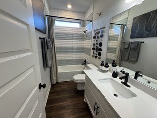 A modern bathroom with wood floors, a white vanity, geometric wall art, and sleek black fixtures.