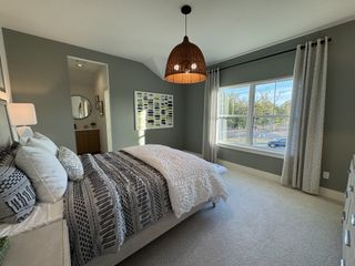 A cozy bedroom with neutral tones, geometric bedding, a large window, and elegant pendant lighting.