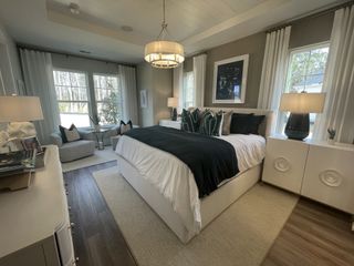An elegant bedroom featuring a luxe bed, modern lighting, large windows, and cozy seating by the window.