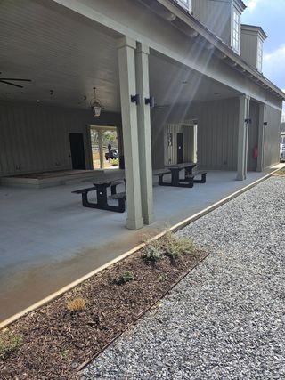 A covered outdoor space features picnic tables, concrete flooring, and light-colored siding, offering a communal gathering area in Harmony by Kinglett Homes (Auburn, GA).