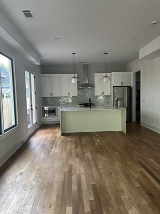A modern kitchen with light wood floors, white cabinets, stainless appliances, and elegant pendant lighting.