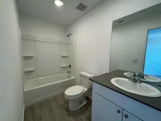 Model Home A modern bathroom featuring a sleek bathtub, wood-style flooring, and a contemporary vanity with ample mirror space.