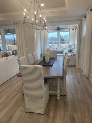 Model Home A chic dining area featuring striped chairs, a wooden table, and an elegant chandelier overlooking a bright window view.