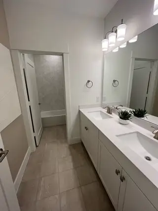 A modern bathroom featuring a dual vanity, spacious mirror, and chic hexagonal-tile bathtub accent wall.