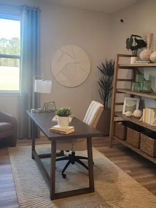 Model Home A cozy home office with a wooden desk, plush chair, and stylish shelving. Neutral tones and natural light enhance its warmth.