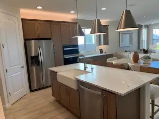 Model Home A modern kitchen featuring stainless steel appliances, sleek pendant lights, and a spacious island with a farmhouse sink.