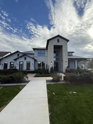 A modern stone and stucco home with landscaped gardens in Travisso Florence Collection by Taylor Morrison (Leander, TX).