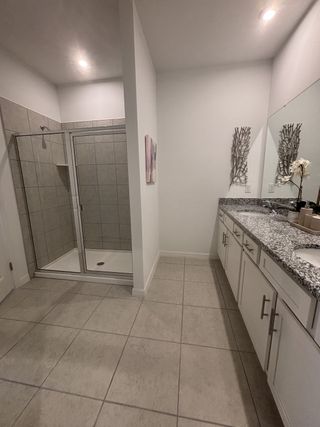 Model Home Spacious bathroom with dual sinks, granite counters, and a glass shower. Minimalist decor with silver accents on the wall.