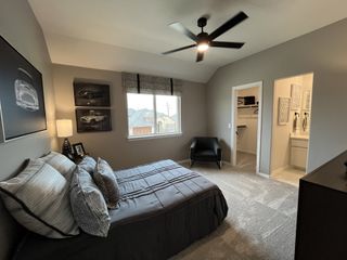 Stylish bedroom with neutral tones, ceiling fan, and car-themed decor. Connected to a walk-in closet and bathroom.