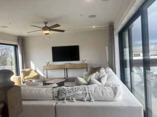 A bright, airy living space features a plush white sectional sofa, a modern entertainment center, and expansive windows offering scenic views.