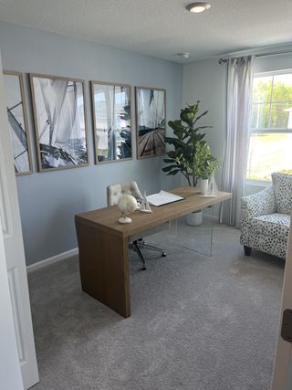 A bright office space features a modern wood and glass desk, framed sailboat prints, and a comfortable patterned armchair, perfect for productivity.