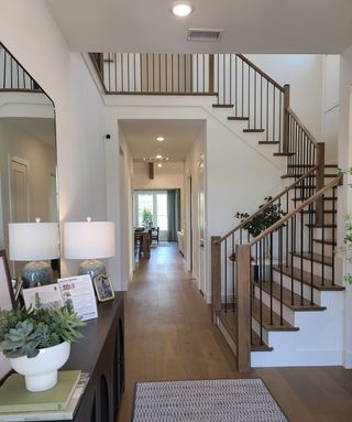 Model Home A modern entryway featuring sleek wooden floors, a staircase with iron railings, and elegant decor accents.