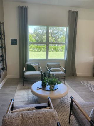 A cozy living area with large windows, comfy armchairs, and a sleek coffee table, complemented by soft curtains and greenery.