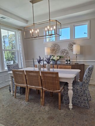 A chic dining room featuring a large table, cane chairs, patterned armchairs, and elegant lighting with decorative accents.