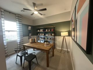 A cozy home office with a wooden desk, modern art, and ample shelving, featuring stylish lighting and a large window.