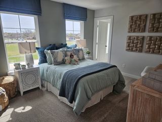 A cozy bedroom featuring a plush bed with blue accents, ample natural light, and stylish decor.