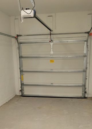 Model Home A spacious garage with a white sectional door and ceiling-mounted opener for convenient vehicle storage.