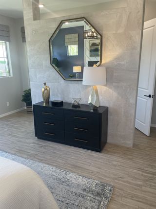 A chic bedroom with a modern black dresser, octagonal mirror, elegant lamp, and stylish decor on wood-textured floors.