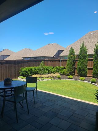 Model Home A cozy patio with a dining set, lush grass, and manicured hedges, perfect for outdoor relaxation.