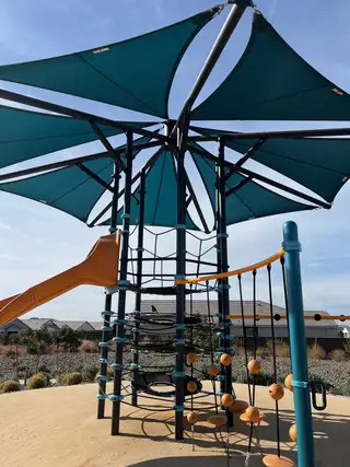 A modern playground with shade sails and climbing structures in Radiance At Superstition Vistas by D.R. Horton (Apache Junction, AZ).
