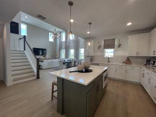 A spacious open-concept kitchen and living area with modern lighting, white cabinetry, and a large island.