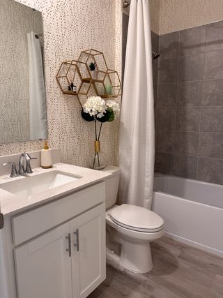 A chic bathroom featuring a vanity, modern fixtures, geometric shelves, and a tiled bathtub.