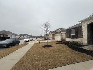 Street view A charming stone-brick home with a manicured lawn in Heartland Signature by KB Home (Heartland, TX).
