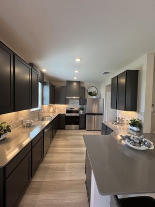 A modern kitchen featuring sleek dark cabinets, stainless steel appliances, and elegant lighting with light wood floors.