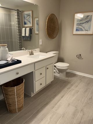A sleek bathroom with wood-style tile flooring, modern vanity, elegant artwork, and a woven wall accent.