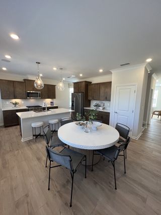 A modern kitchen with dark wood cabinets, a sleek round table, and stylish lighting above a spacious island.