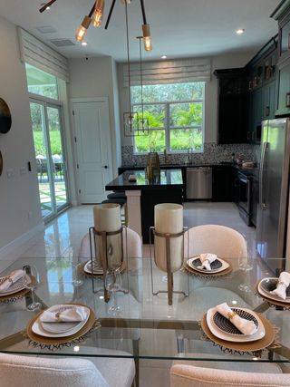 A chic dining area with a glass table, elegant place settings, and a modern chandelier overlooking a lush green view.