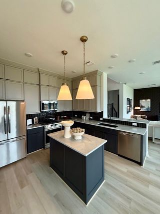 A modern kitchen with sleek cabinets, a central island, stainless steel appliances, and elegant pendant lighting.