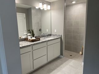 A modern bathroom with a granite countertop, dual sinks, and a spacious tiled shower, complemented by sleek lighting.