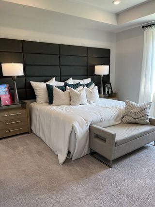 A cozy bedroom featuring a plush upholstered headboard, elegant lamps, and a chic bench, creating a serene retreat.